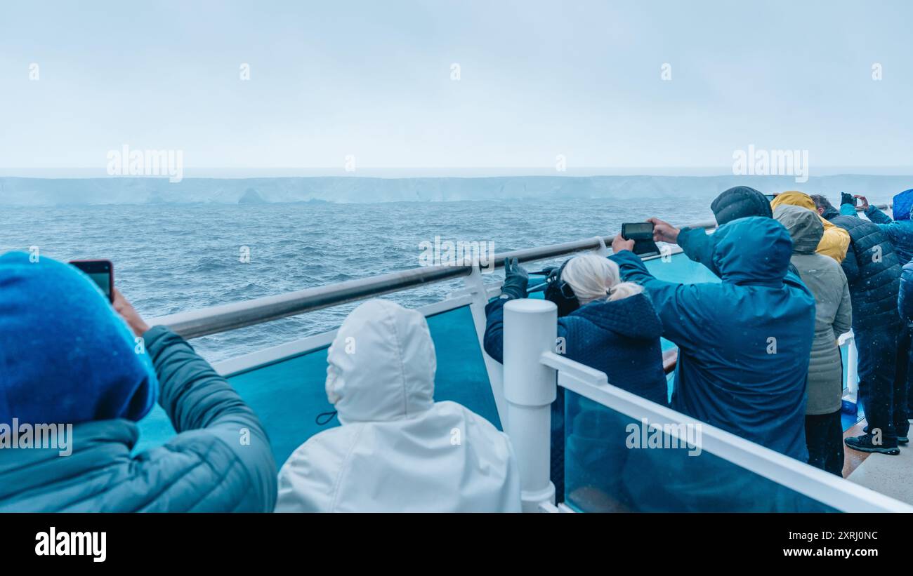 Antartide - 26 dicembre 2023 - foto di A23a Iceberg dalla nave da crociera dietro folla. I passeggeri reggono i cellulari per fotografarlo Foto Stock