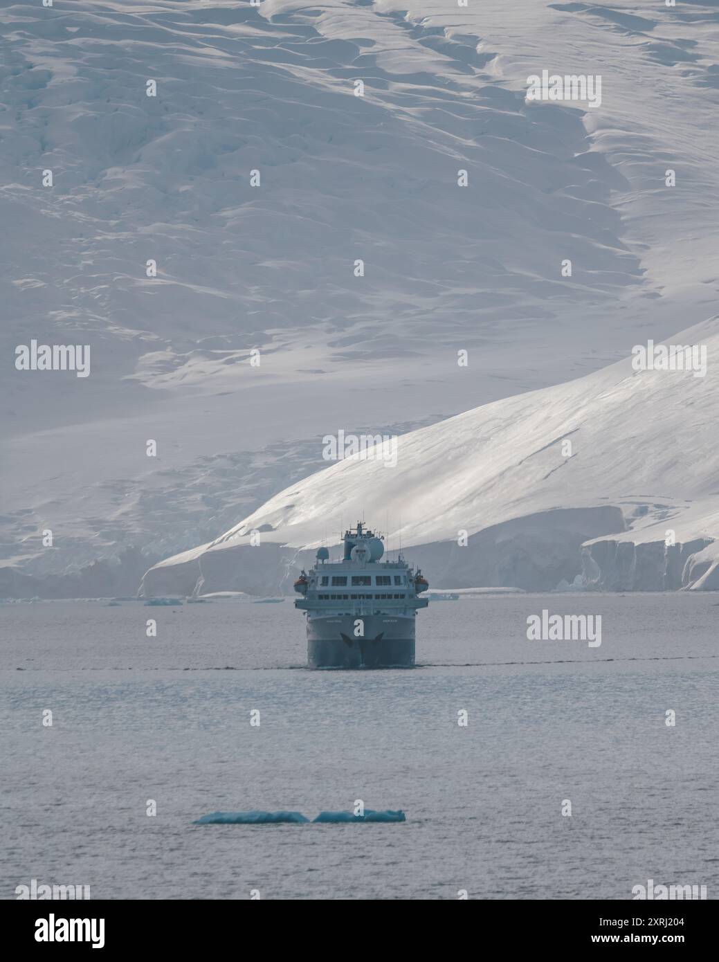 Nave da crociera Antartide Expedition in navigazione verso di noi con l'enorme parete di ghiaccio del Ghiacciaio dietro di essa. Iceberg nell'oceano. Tour turistico di Remote Adventure Travel Foto Stock