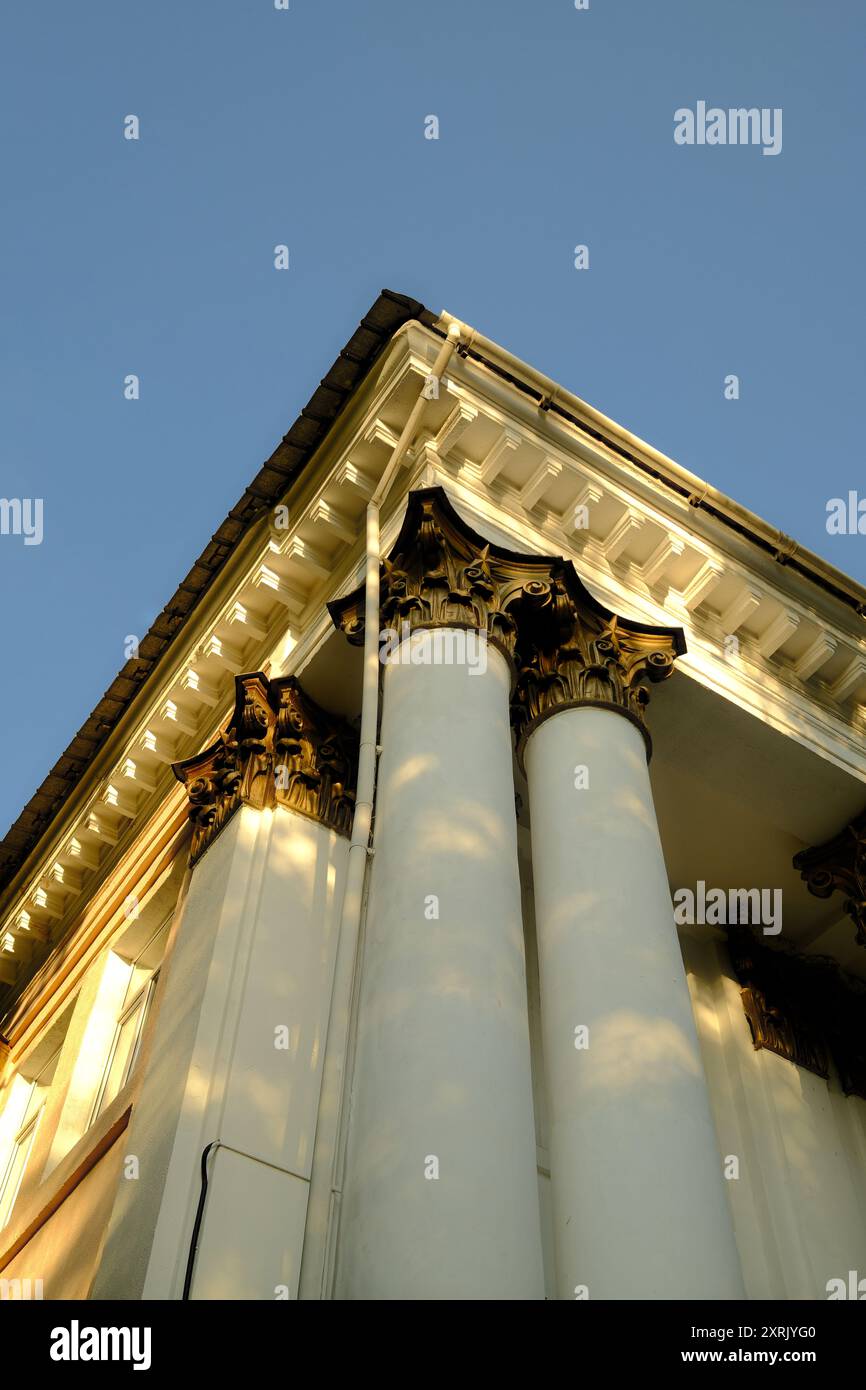 Maestoso edificio neoclassico con colonne bianche ornate e capitelli corinzi dorati sotto la calda luce del sole Foto Stock