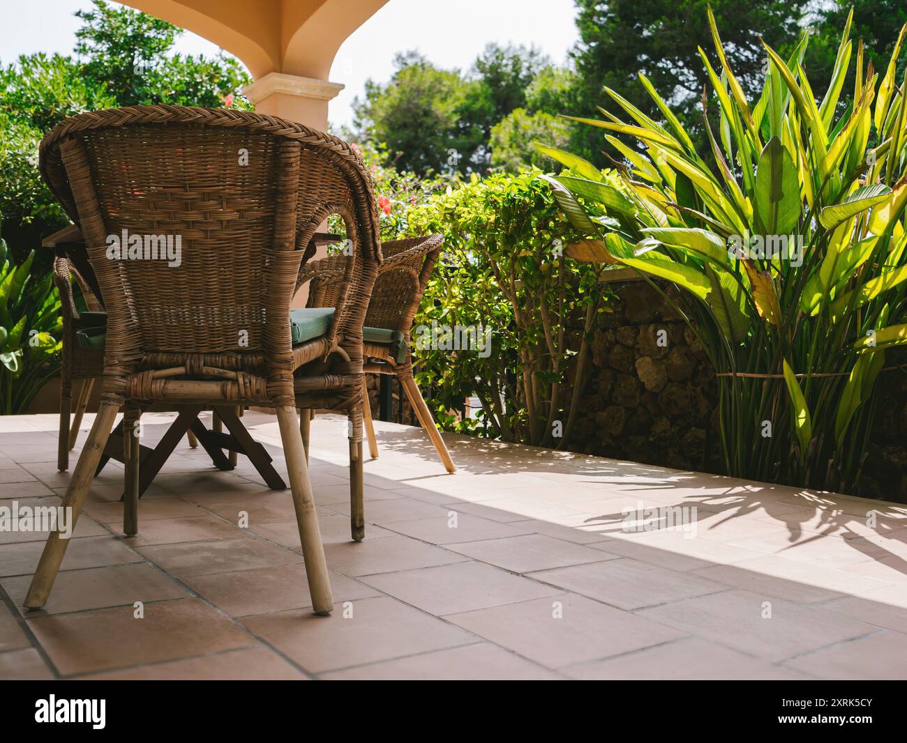 Un lussuoso patio con foglie di banana e un bellissimo giardino sullo sfondo, con una sedia e un tavolo annodati in legno, creando un ambiente sereno ideale per lavorare in remoto e rilassarsi in un ambiente lussuoso Foto Stock