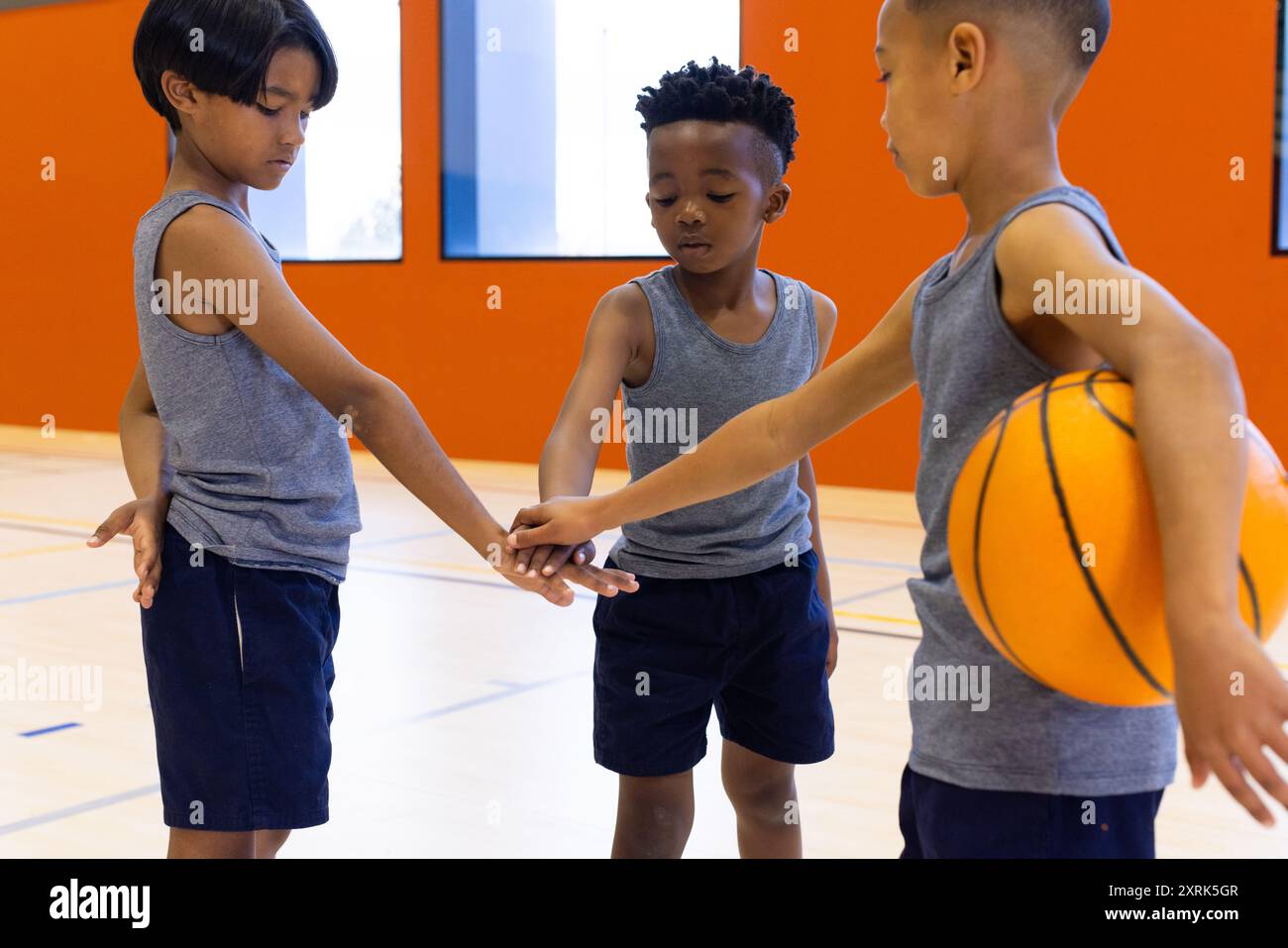 Nella palestra scolastica, i ragazzi in abbigliamento sportivo si accoccolano con il basket, si preparano per la partita. lavoro di squadra, allenamento, palestra, huddle, energia, concorrenza Foto Stock