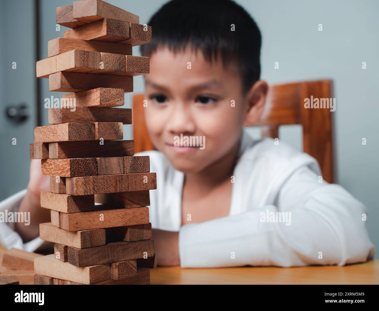 Allegro ragazzo asiatico che gioca con i blocchi di legno Jenga, divertendosi e imparando la creatività, concetto intelligente per bambini, pianificazione dei blocchi di legno, rischio e S. Foto Stock