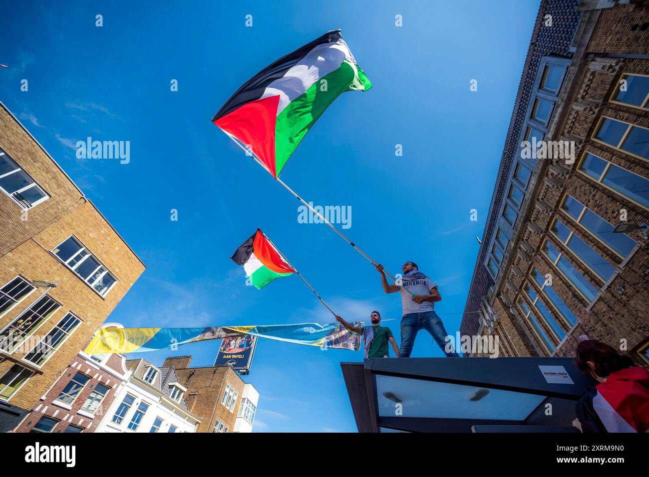 Due manifestanti maschili inondano bandiere nazionali sul tetto della fermata dell’autobus, durante la dimostrazione “MAI PIÙ È ORA”. Una piccola manifestazione a Utrecht è quella di riportare ancora una volta alla ribalta la situazione del popolo palestinese a Gaza e il continuo genocidio perpetrato su di esso dall'IDF (forza di difesa israeliana). Mentre i leader occidentali cantano ancora la stessa questione del diritto di auto-sfida di Israele in una terra occupata. Il Ministero della salute a Gaza dal 9 agosto, afferma che almeno 39.699 persone sono morte, tra cui più di: 15.000 bambini uccisi. Feriti: Più di 91.722 e 10.000 missin Foto Stock