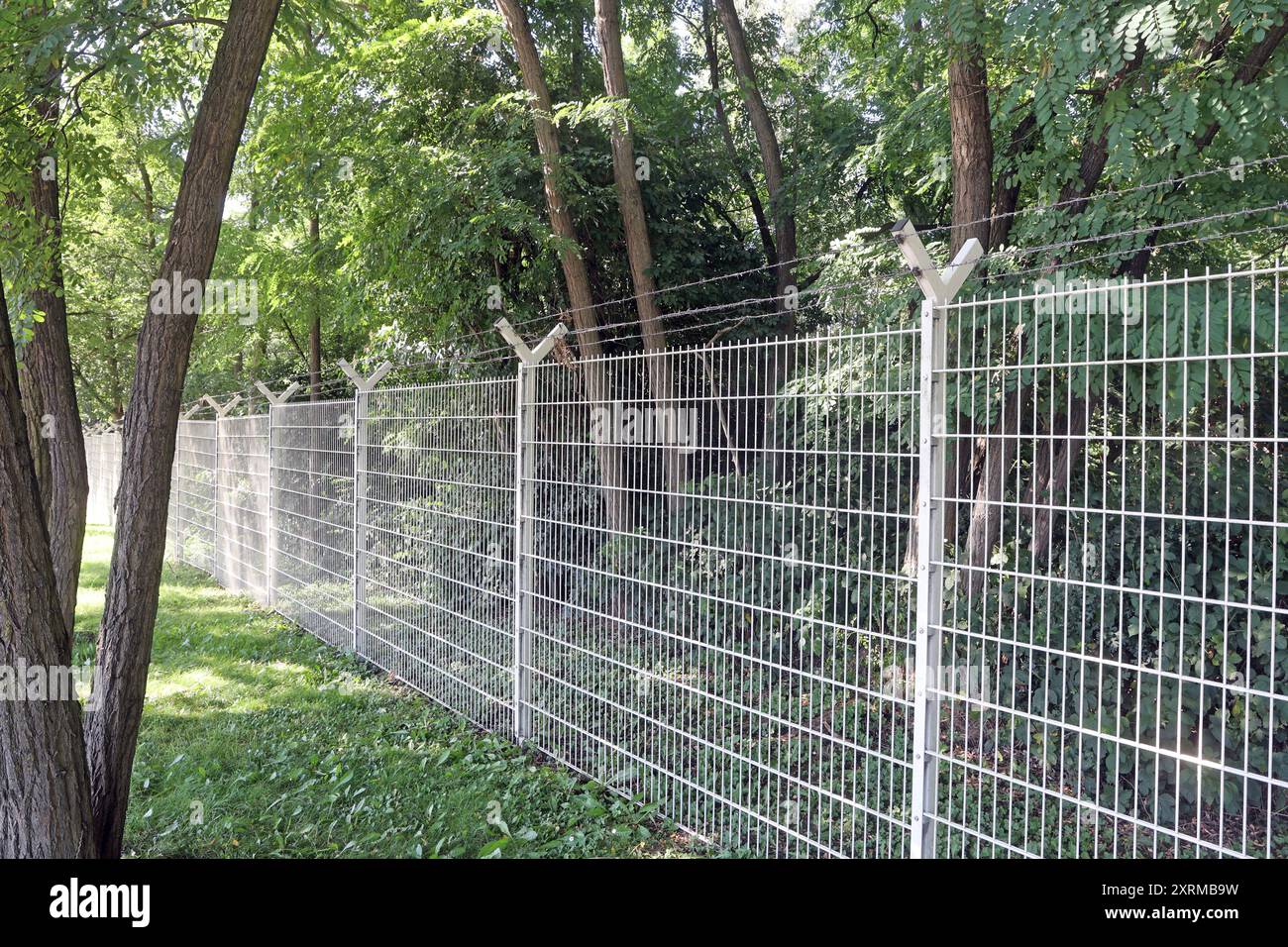 Zäune aus massiven materiale Ein unbeschichteter Stahlmattenzaun mit Stacheldraht am oberen Ende als Schutz an einem Gewerbegebiet *** recinzioni in materiale solido recinzione in rete di acciaio non rivestito con filo spinato nella parte superiore come protezione in una zona industriale Foto Stock