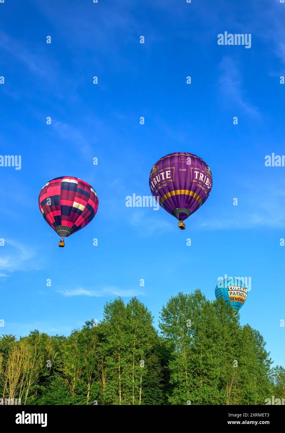 Palloncini colorati illuminati dal sole nell'ora d'oro, dalla festa in mongolfiera di Bristol del 2024 mentre passano sopra gli alberi vicino a Siston; Bristol. Scattate alle 19.45, sabato Foto Stock