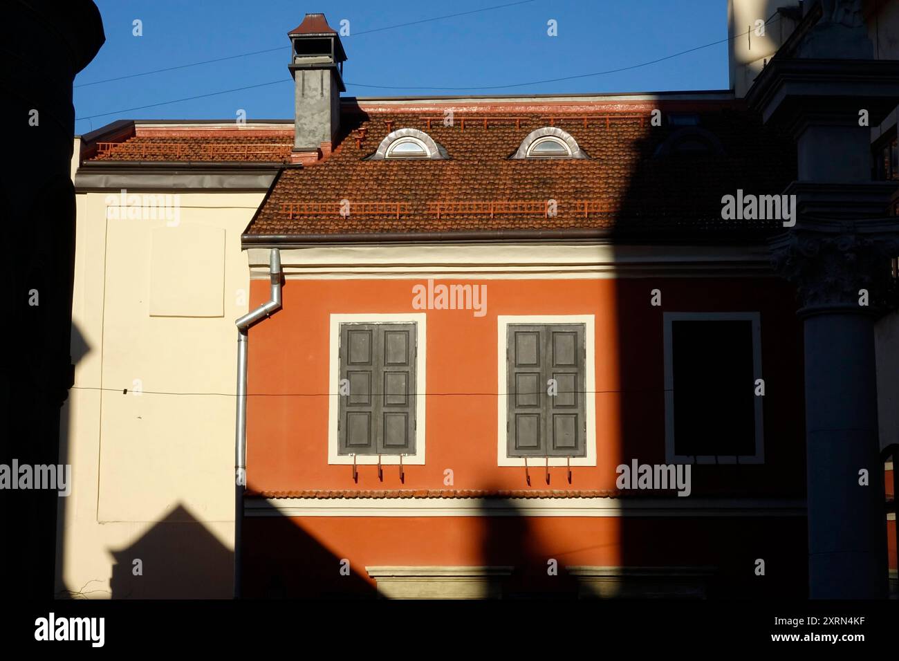 Un vivace edificio rosso sorge nel cortile armeno di Leopoli, che getta ombre mentre la luce del sole illumina le sue caratteristiche architettoniche uniche. Foto Stock