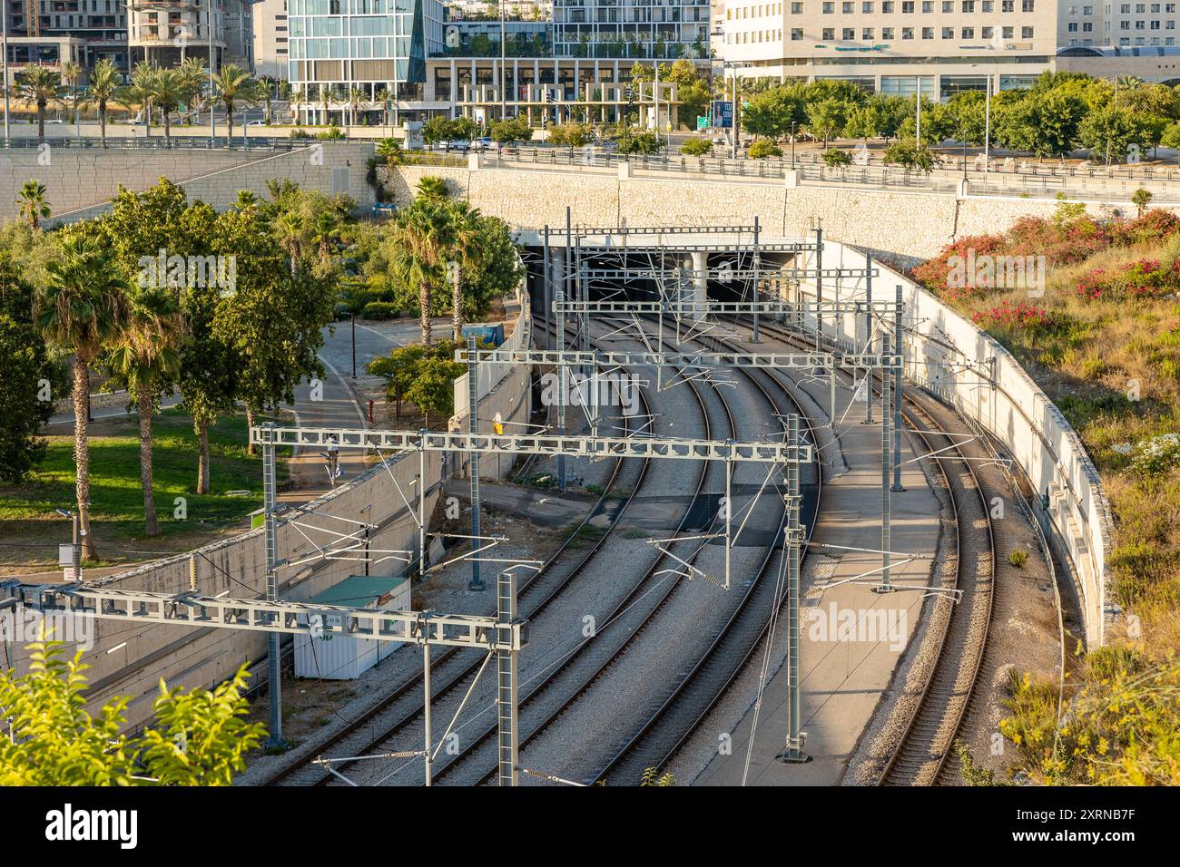 Modiin, Israele, 3 agosto 2024. Binari ferroviari che conducono ad un tunnel sotterraneo. Parco cittadino e moderna architettura urbana Foto Stock