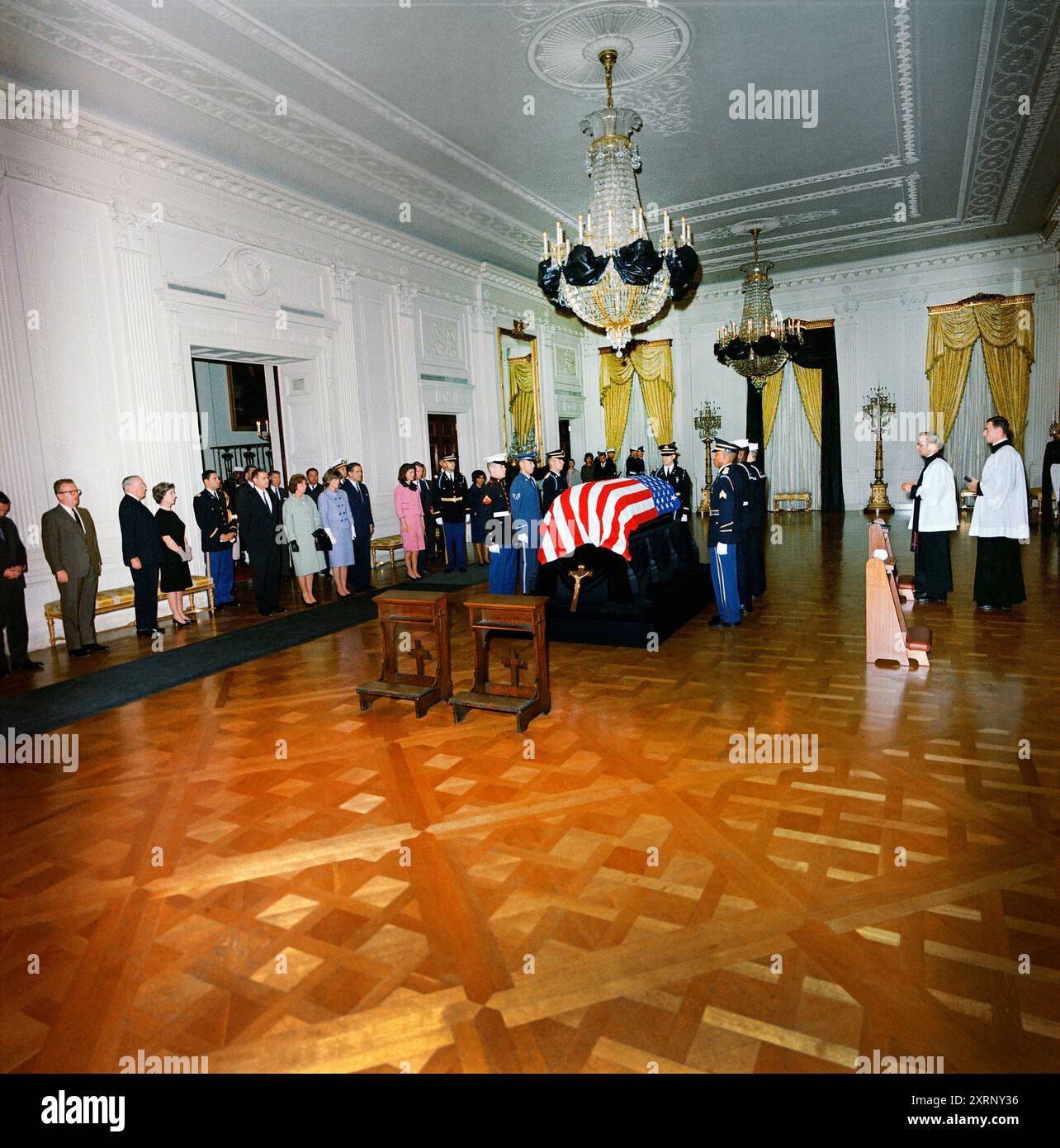 Bara drappeggiata di bandiera del defunto presidente degli Stati Uniti John Kennedy, First Lady Jacqueline Kennedy, Procuratore generale, Robert Kennedy, Jean Kennedy Smith, Ethel Skakel Kennedy, R. Sargent Shriver, Janet Auchincloss, Hugh D. Auchincloss; Segretario della difesa, Robert S. McNamara, tra gli altri in lutto, East Room, Casa Bianca, Washington, D.C., USA, Robert Knudsen, White House Photographs, 23 novembre 1963 Foto Stock