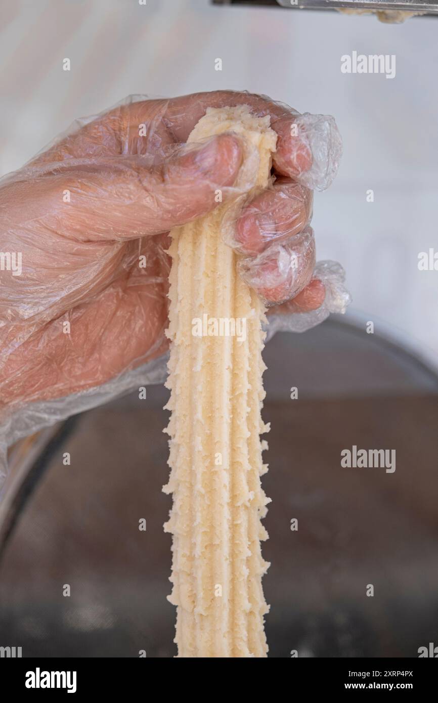 Donna che mette l'impasto di churros crudo in olio caldo per friggerlo 1. Foto Stock