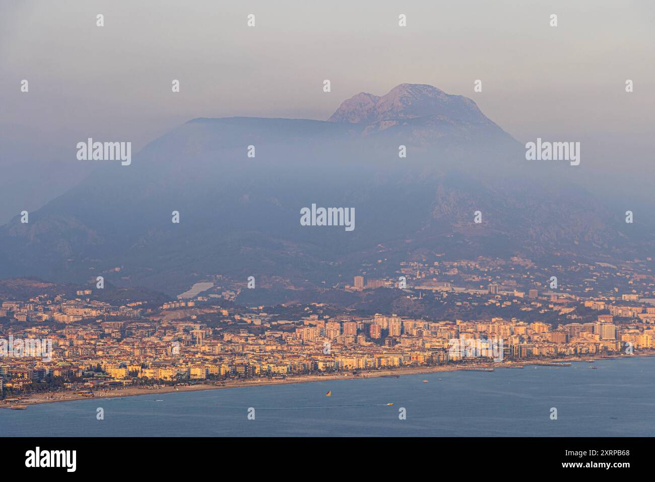 Die Stadt Alanya Türkei am Abend Dichter Dunst hängt am Abend an den Bergen hinter der Stadt Alanya. Die Luftfeuchtigkeit ist in Dieser Region an der Türkischen Riviera durch die im Sommer hohen Temperaturen, das Meer und das dahinter Steil ansteigende Taurusgebirge häufig sehr hoch. Alanya Antalya Türkei **** la città di Alanya Turchia la sera densa foschia è appesa sulle montagne dietro la città di Alanya l'umidità è spesso molto elevata in questa regione della riviera turca a causa delle alte temperature estive, il mare e le ripide montagne del Tauro alle sue spalle, Alany Foto Stock