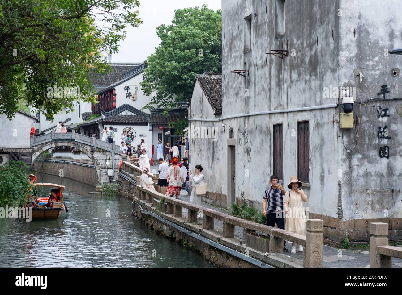 Suzhou, Cina - 11 giugno 2024: Un canale attraversa un pittoresco quartiere storico di Suzhou. La gente passeggia lungo il sentiero di pietra, una barca scivola Foto Stock