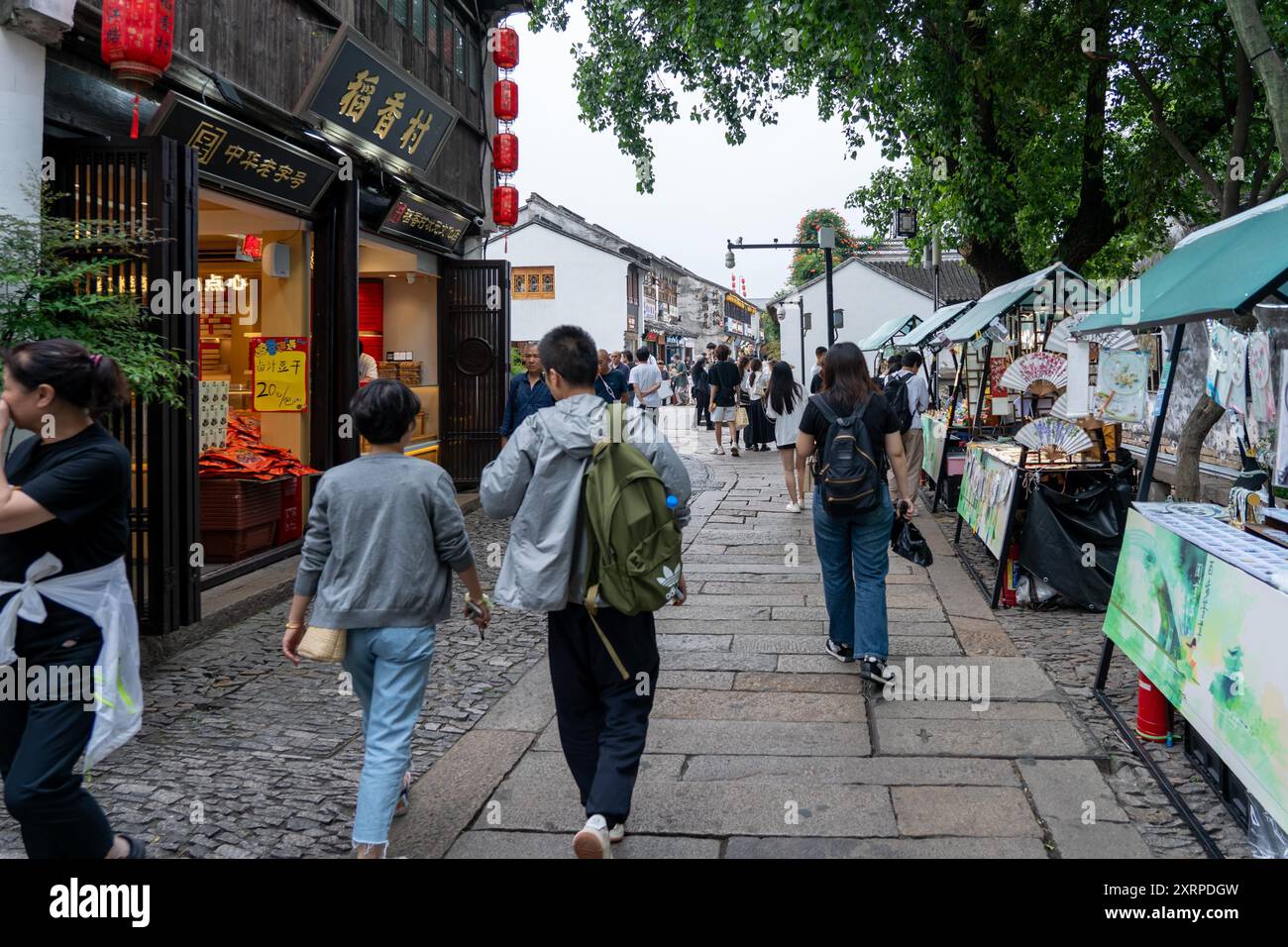 Suzhou, Cina - 11 giugno 2024: Una stretta strada acciottolata a Suzhou, Cina, fiancheggiata da negozi tradizionali e bancarelle del mercato. Foto Stock