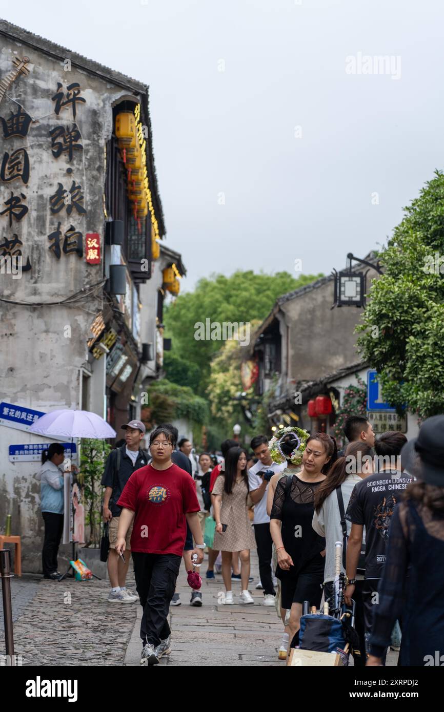 Suzhou, Cina - 11 giugno 2024: Una folla di persone cammina lungo una stretta strada di pietra fiancheggiata da tradizionali edifici cinesi a Suzhou, in Cina. Foto Stock