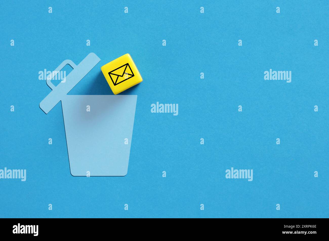 Il cubo giallo con il simbolo di un'e-mail sta cadendo in un cestino blu su sfondo blu. Immagine dell'eliminazione delle e-mail. Posta indesiderata. Foto Stock