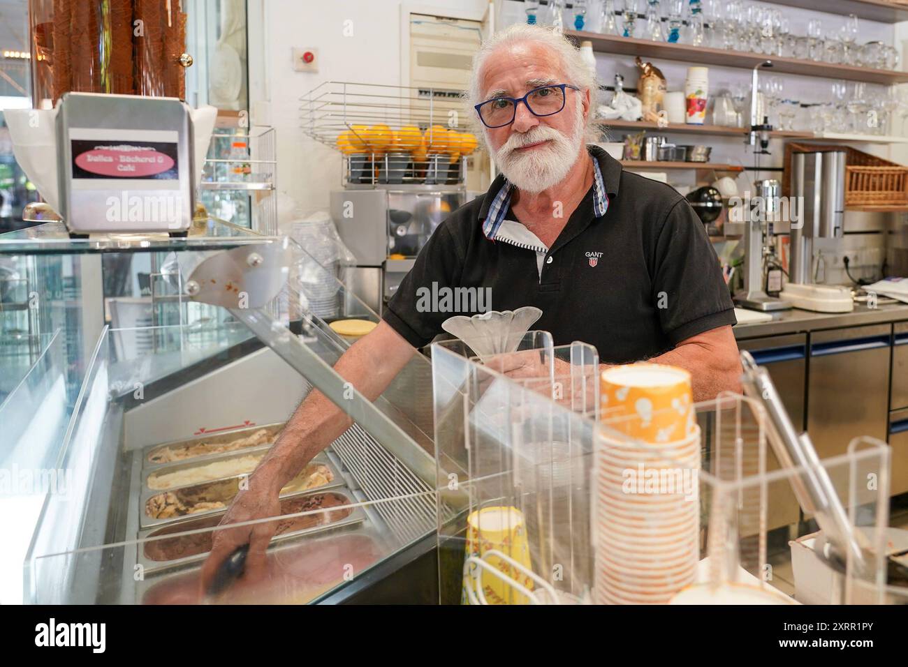 Emilio Menno serviert Eis im Dalles Cafe. Auch er klagt über das zunächst schlechte Wetter und hofft auf ein gutes Geschäft im Spätsommer nach den Ferien - Mörfelden-Walldorf 11.08.2024: Eissaison in der Doppelstadt *** Emilio Menno serve gelati al Dalles Cafe si lamenta anche del maltempo iniziale e spera in buoni affari a fine estate dopo le vacanze Mörfelden Walldorf 11 08 2024 stagione dei gelati nella città gemella Foto Stock