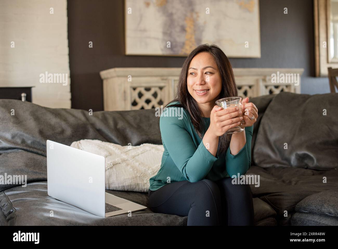 Donna rilassata che tiene la tazza seduta sul divano Foto Stock