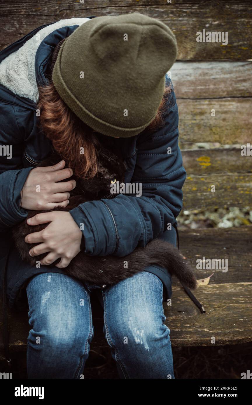 Adolescente in abiti vecchi purtroppo tiene e abbraccia il gatto nero in grembo Foto Stock