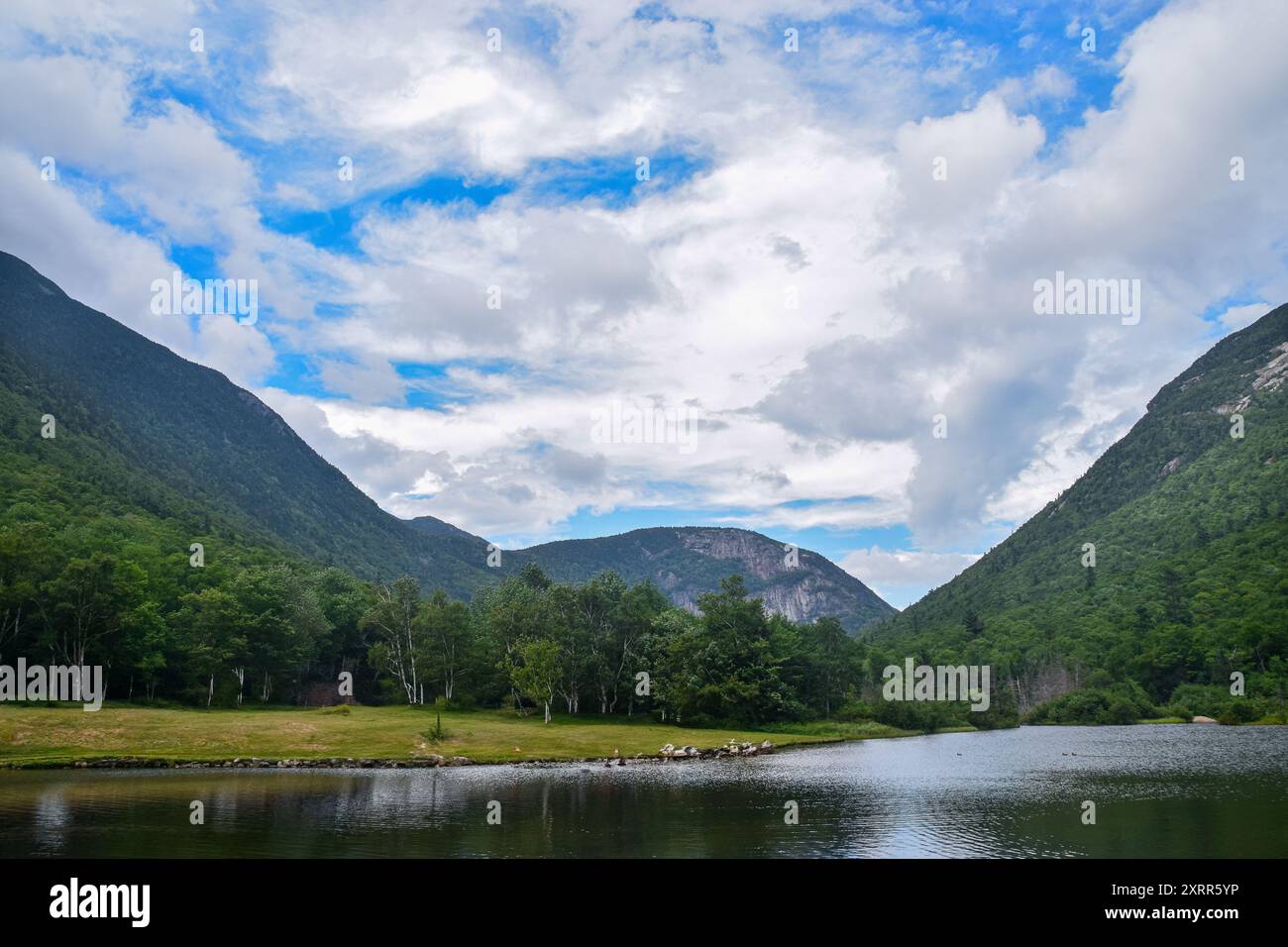 Tranquillo lago circondato da lussureggianti montagne verdi e un cielo blu. Foto Stock