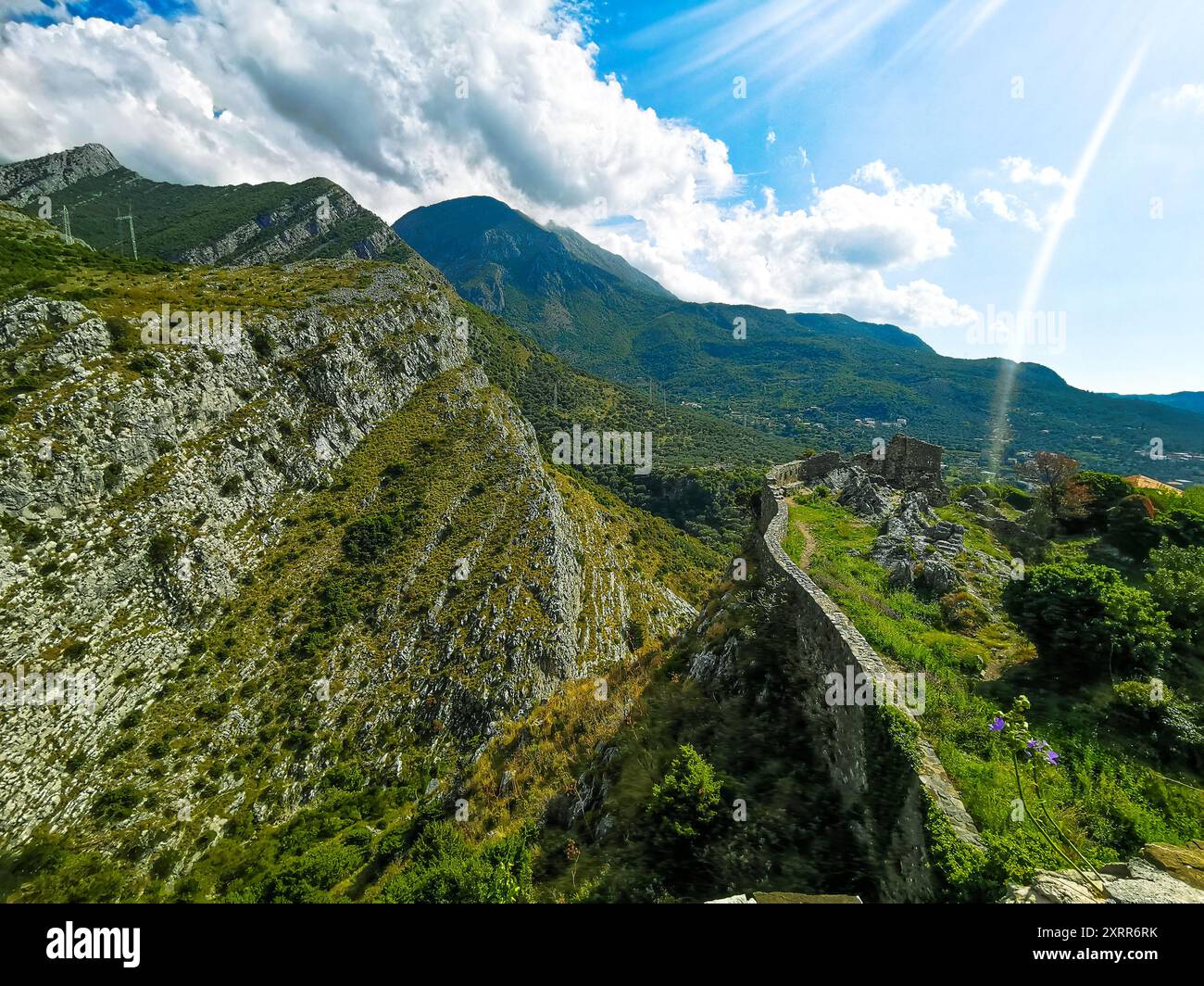 Vecchie rovine a Cattaro con montagne, cieli blu e raggio di sole Foto Stock