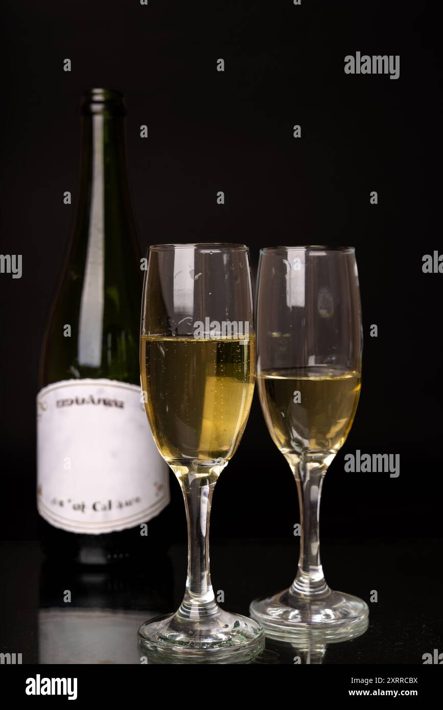 Uno shot verticale di una bottiglia di champagne e due bicchieri pieni di bollicine su sfondo nero, perfetto per feste, Natale o Capodanno Foto Stock