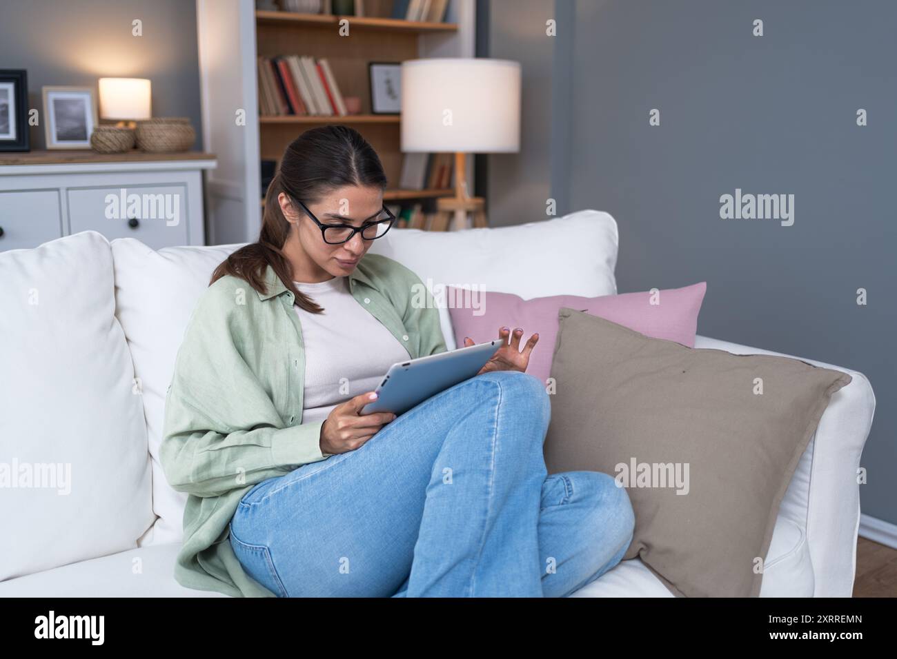 Una giovane donna caucasica rilassata ha letto un libro su un lettore di dispositivi moderni comodamente seduto sul divano di casa Ritratto di persone belle Foto Stock