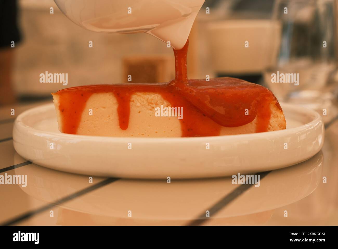 Una fetta di cheesecake con salsa di fragole. La cheesecake viene servita su un piatto bianco e viene posta su un tavolo di legno Foto Stock