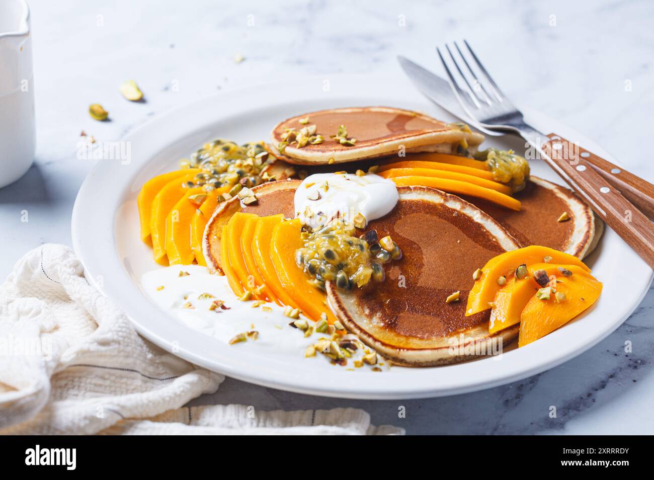 Pancake per colazione con mango e frutta della passione su un piatto bianco. Ricetta vegana sana. Foto Stock