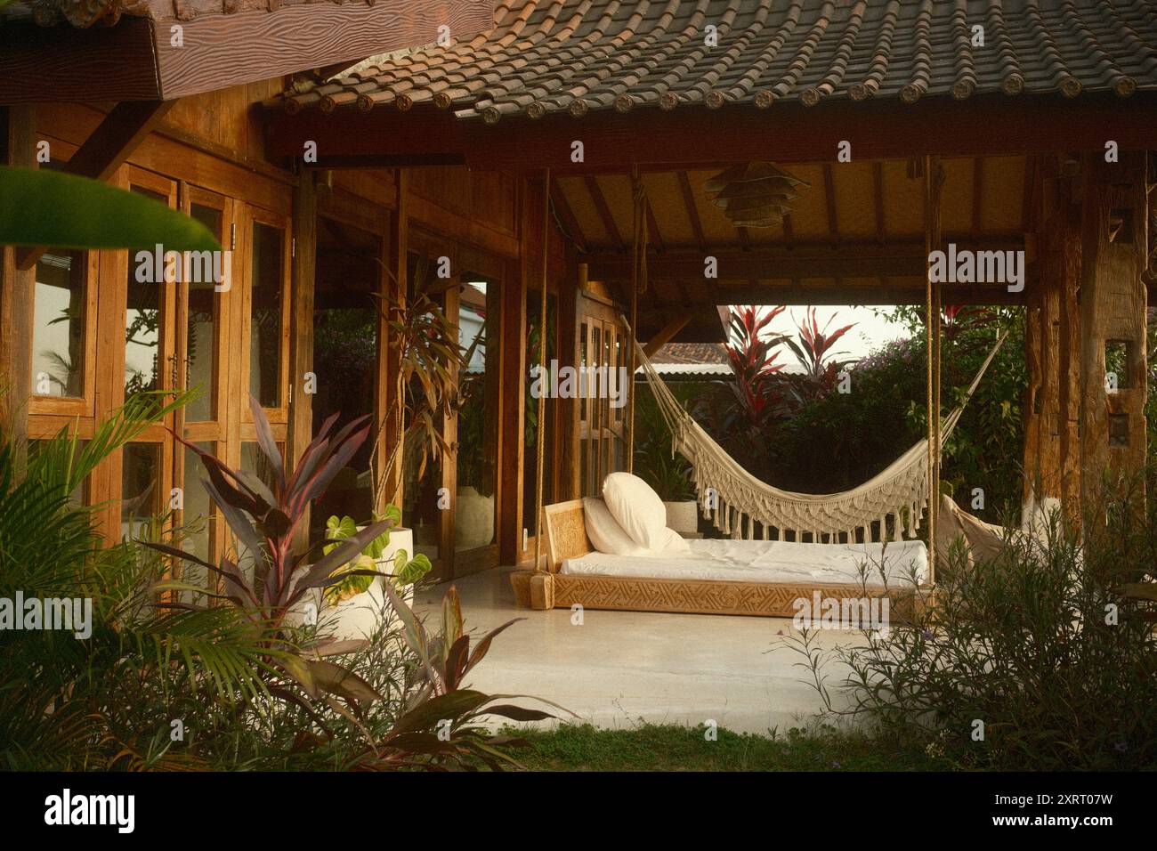 Tabanan, Bali, Indonesia - 9 agosto 2024: Terrazza patio di una moderna villa in legno in stile rustico con mobili da esterno, un letto altalena e un mac Foto Stock