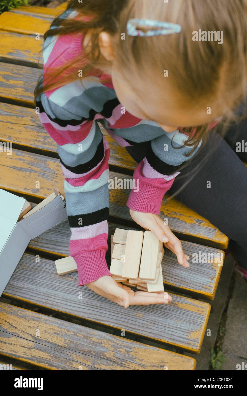 Persona che impilava blocchi di legno, costruiva la torre mentre era seduto a un tavolo all'aperto, concentrandosi sul bilanciamento dei pezzi. Primo piano Foto Stock