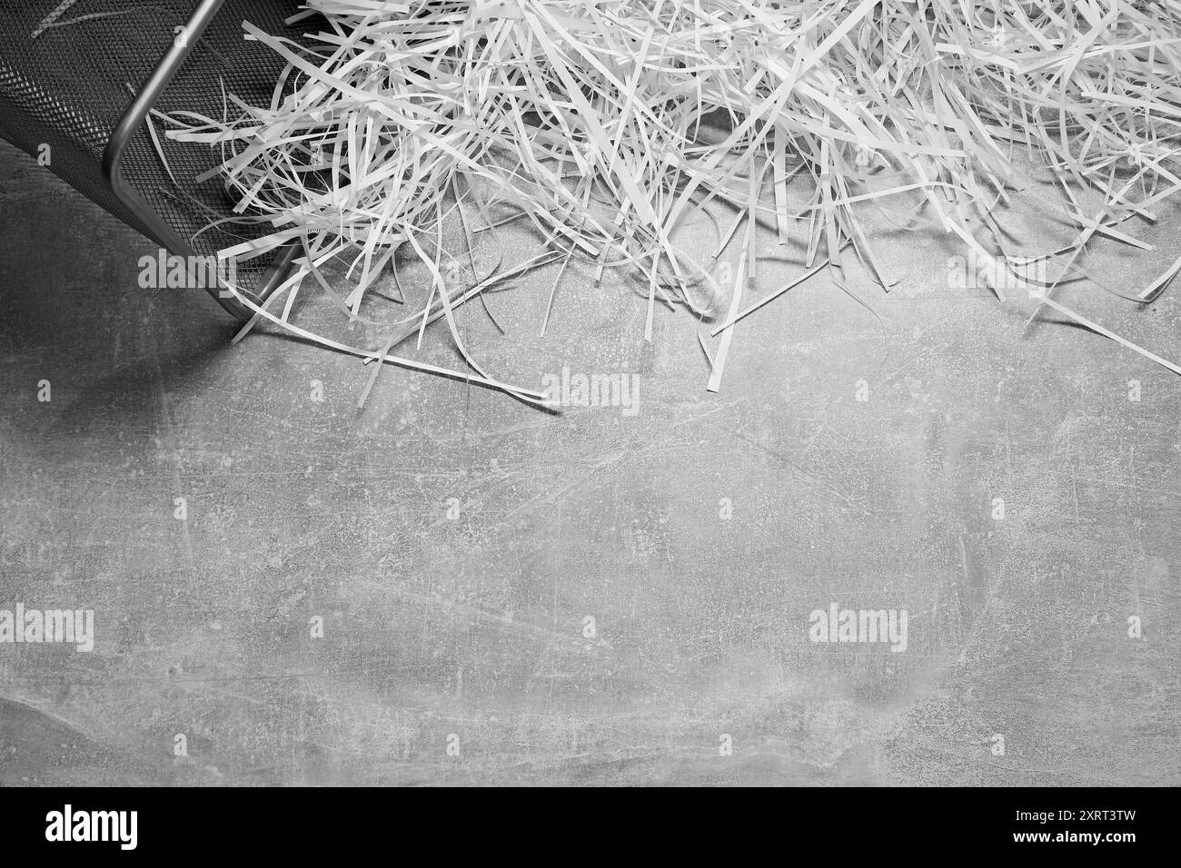 Strisce di carta triturata con cestino su un tavolo con trama grigia, vista dall'alto. Spazio per il testo Foto Stock