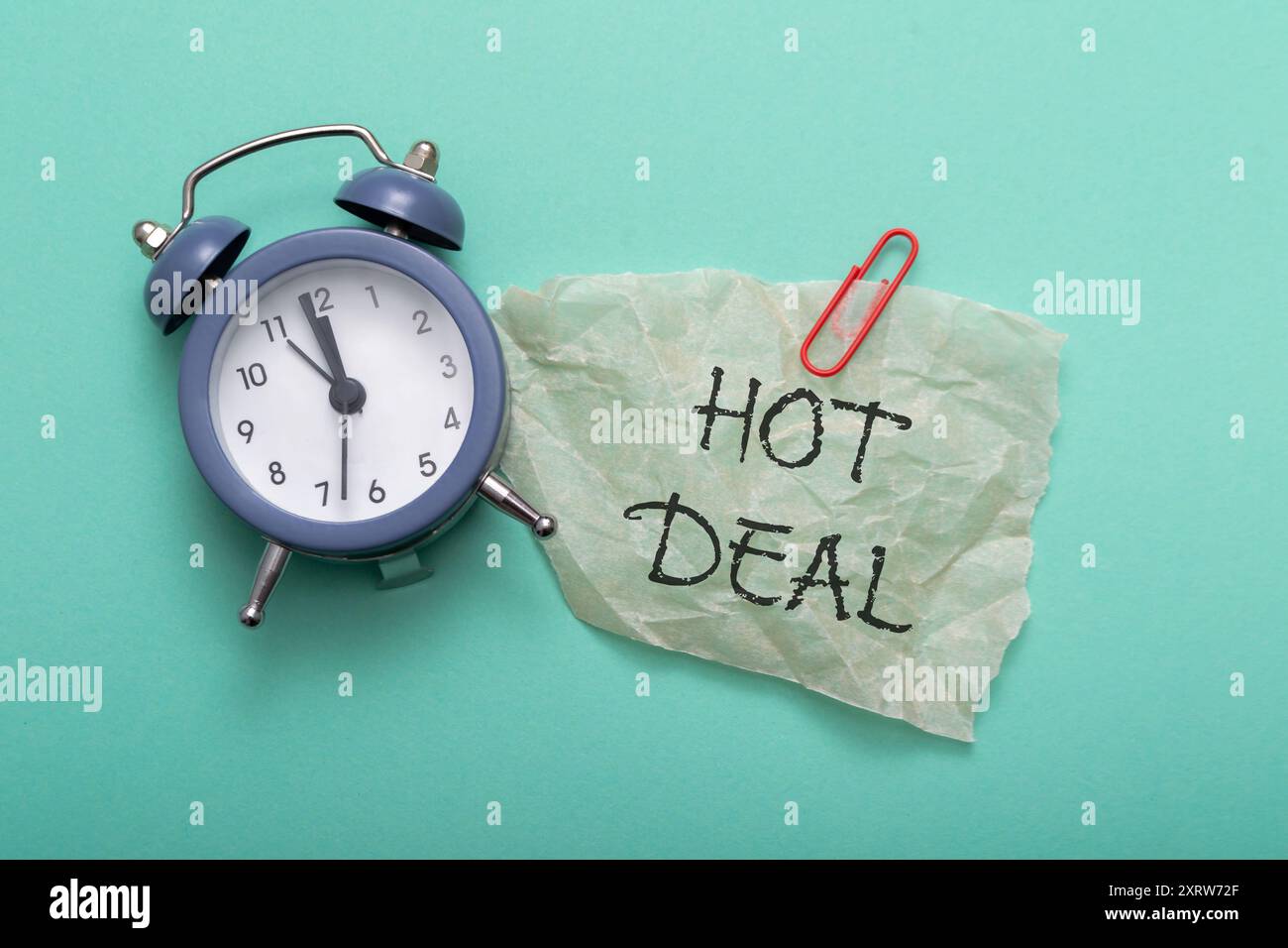 Un orologio con le mani sui numeri 3 e 9. Un pezzo di carta con scritto sopra la parola "HOT DEAL" Foto Stock