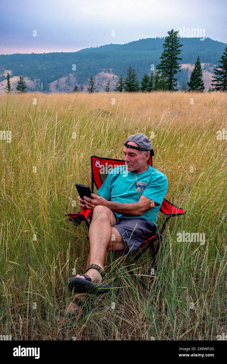 Un maschio in pensione si rilassa dopo una giornata di arrampicata e legge un libro sul suo Kindle. Blue Mountains, Oregon Foto Stock