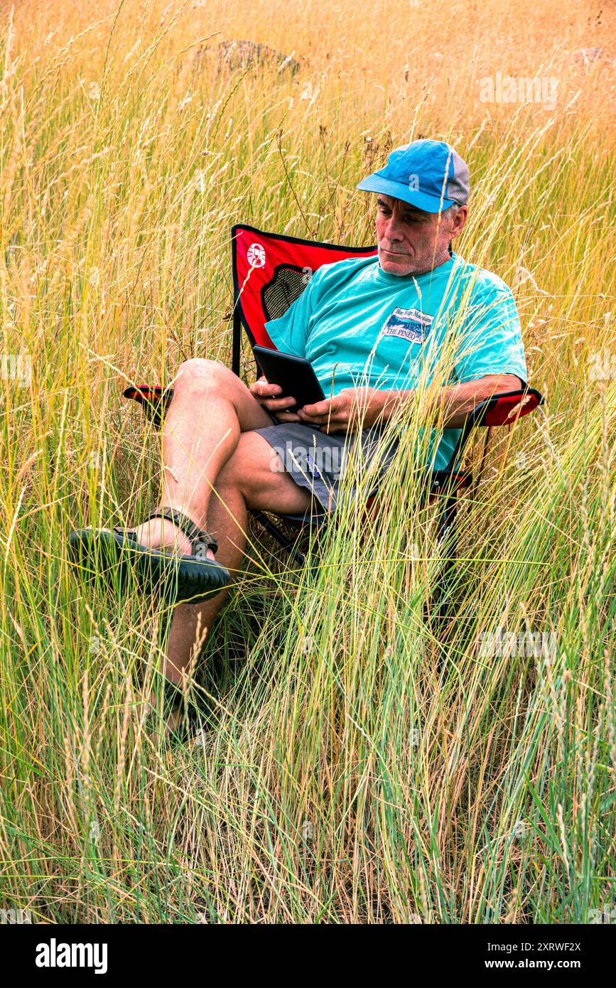 Un maschio in pensione si rilassa dopo una giornata di arrampicata e legge un libro sul suo Kindle. Blue Mountains, Oregon Foto Stock