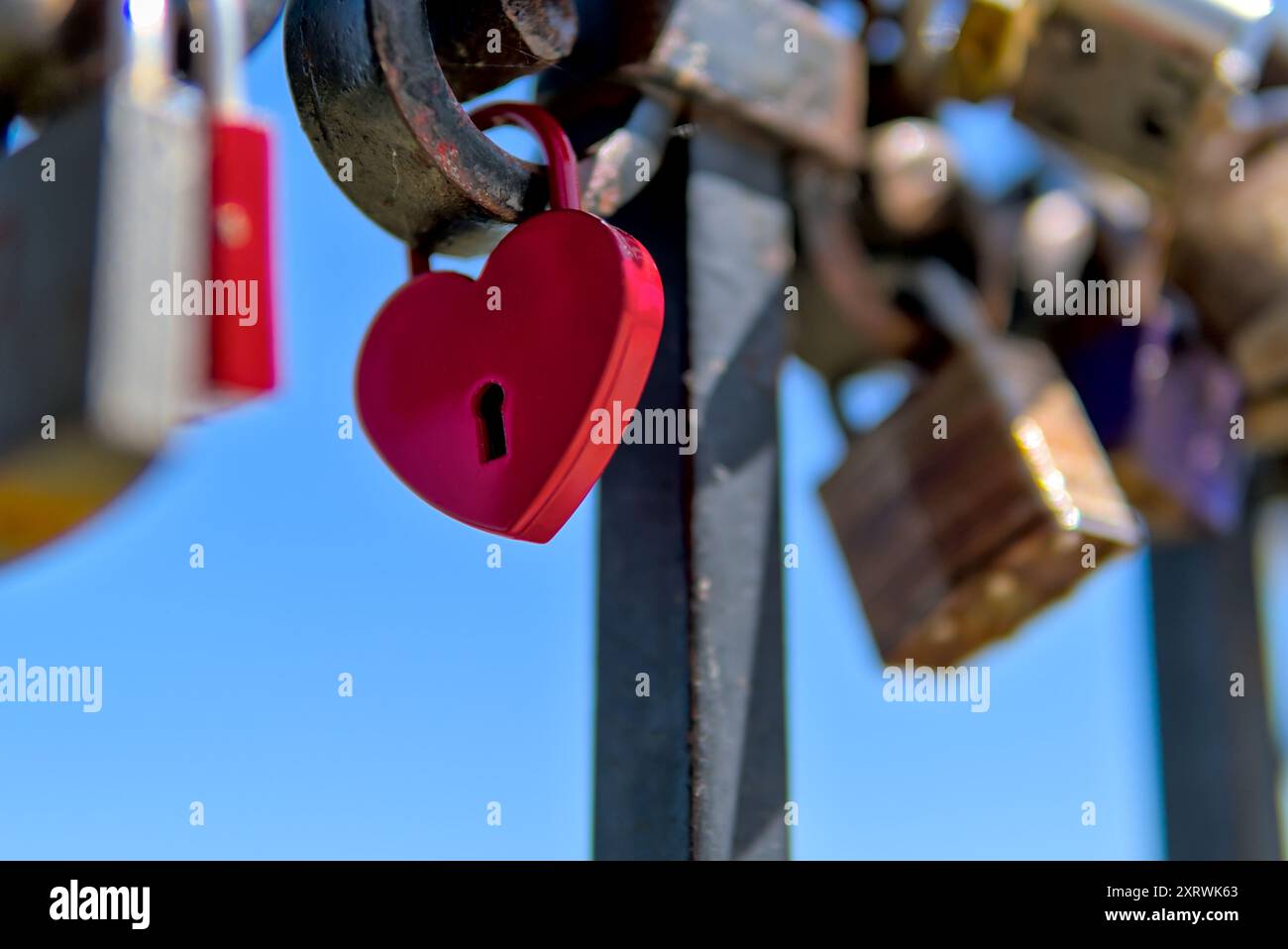 Lucchetto rosso a forma di cuore che simboleggia l'amore, attaccato ad una ringhiera tra gli altri lucchetti in una giornata di sole. Foto Stock
