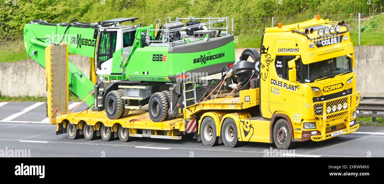 Appaltatori Scania e Yellow con semi-rimorchio a pala bassa carica nuova macchina per movimentazione materiali Sennebogen 835E tedesca che guida l'autostrada M25 Essex Inghilterra Regno Unito Foto Stock