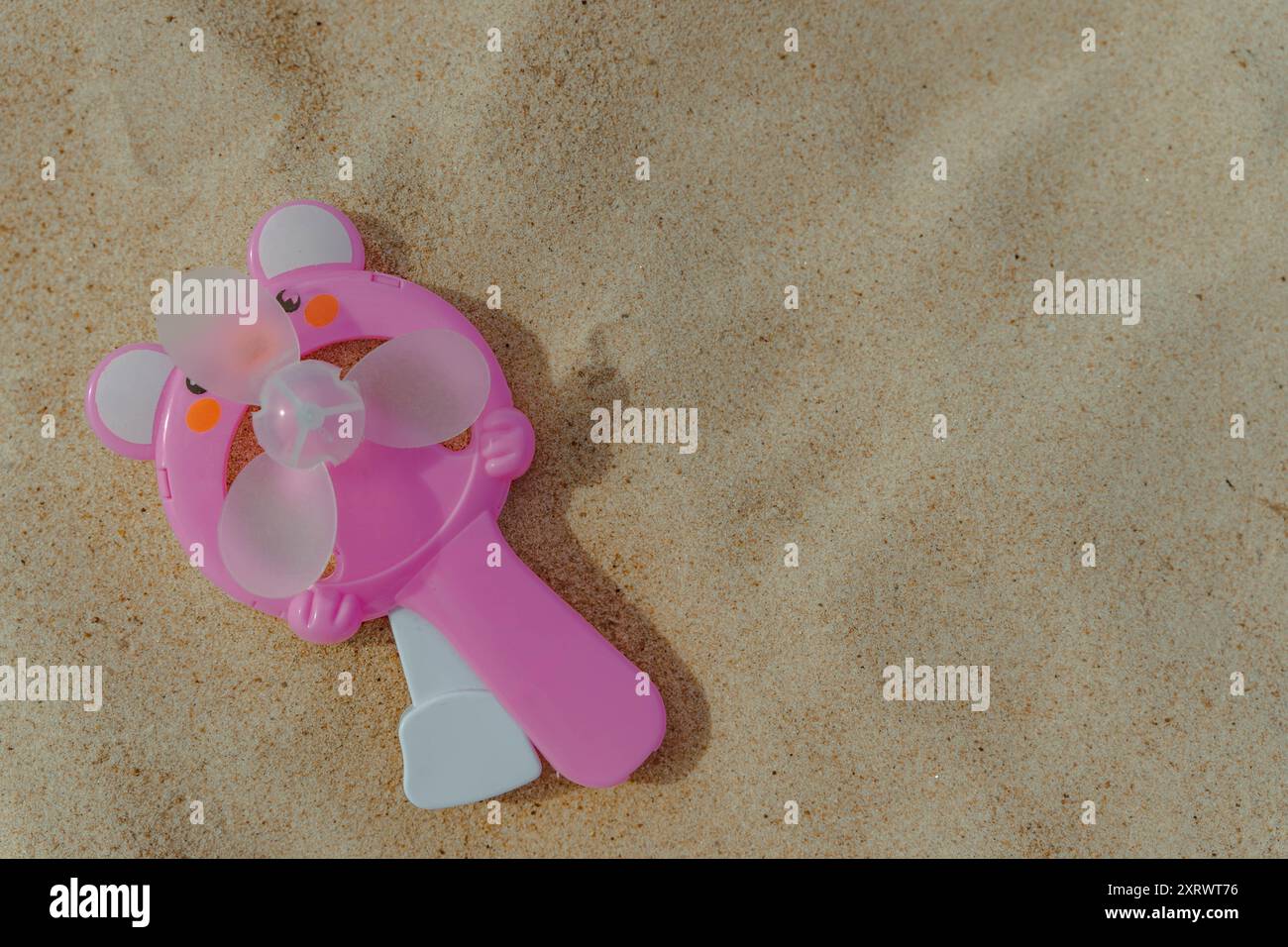 Un ventilatore palmare rosa giace sulla sabbia soffice della spiaggia. Foto Stock