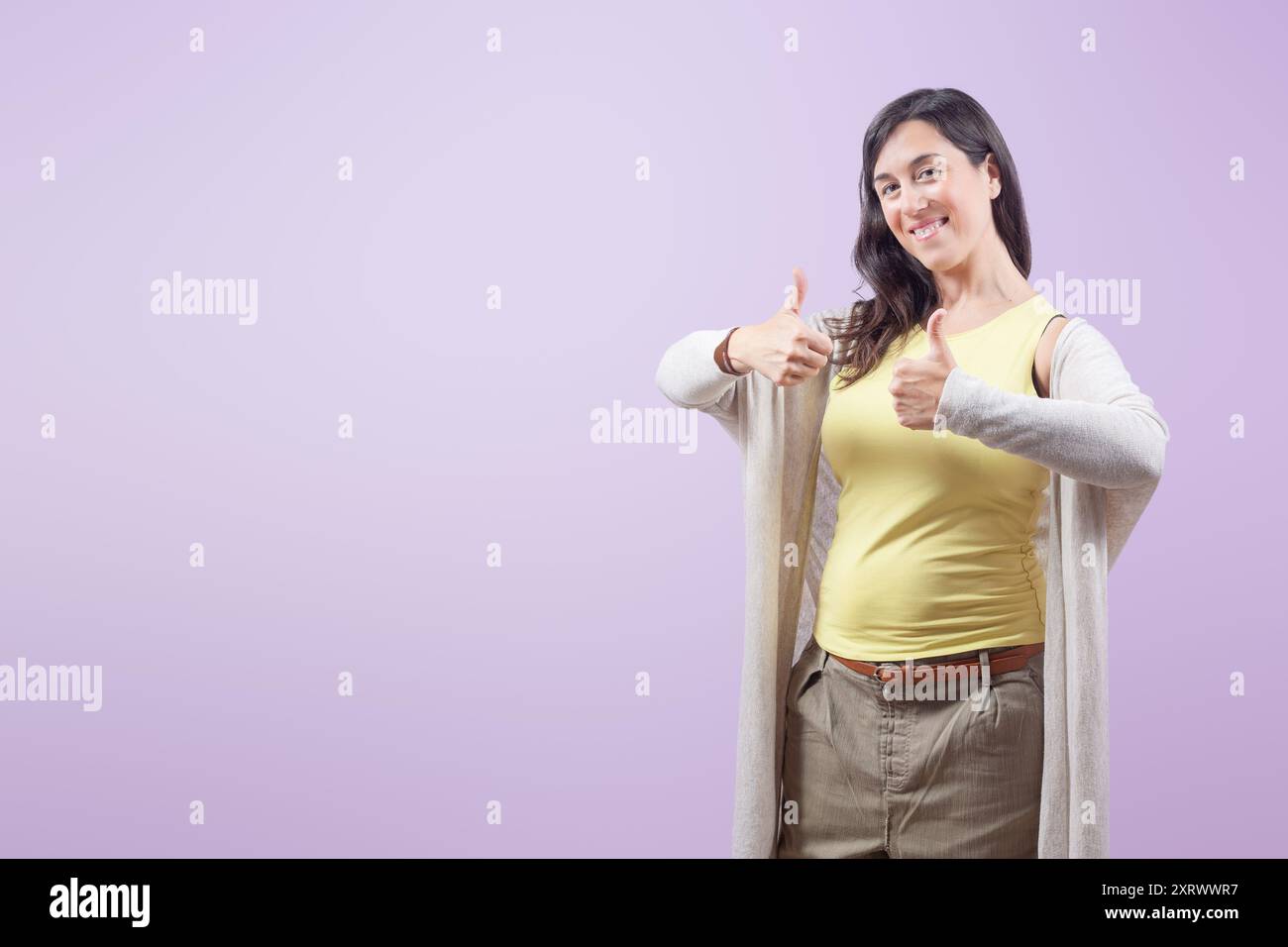 Ritratto di una giovane donna d'affari felice e sicura di sé che mostra due pollici su sfondo viola isolato Foto Stock