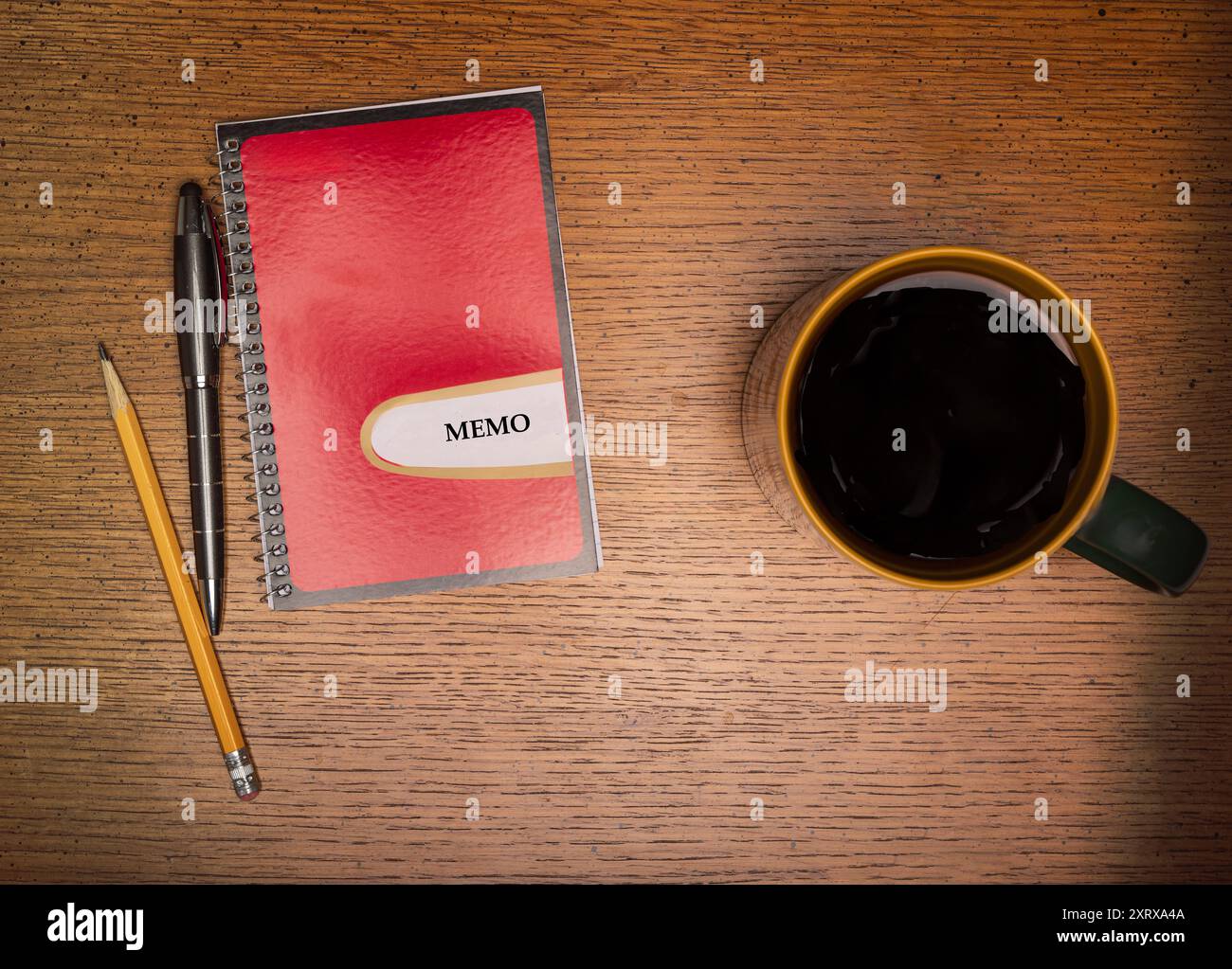 Caffè in tazza dorata su un tavolo di legno accanto a un libro di memo rosso e oro con penna e matita Foto Stock