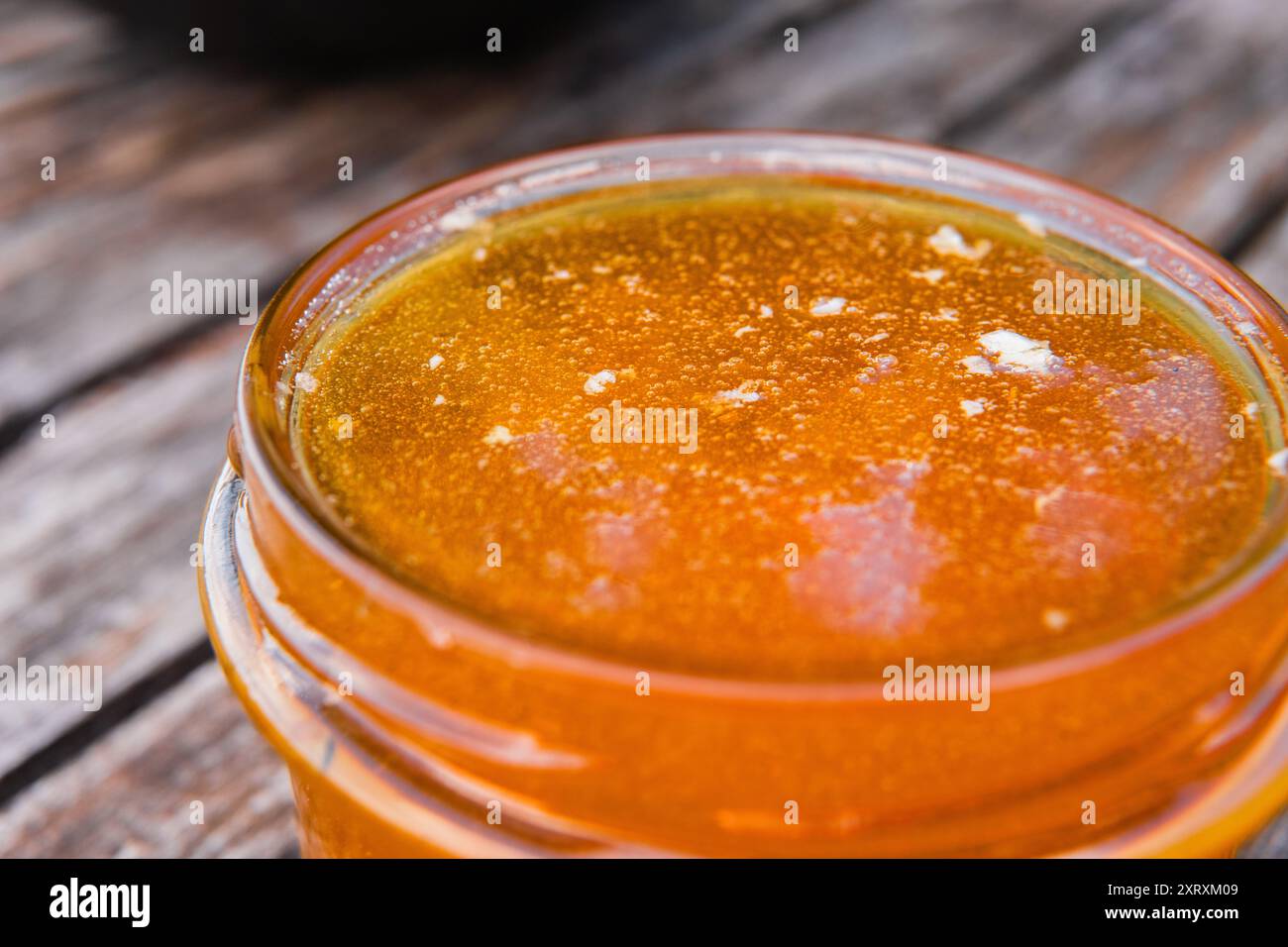 Barattolo di miele riempito fino all'orlo con miele fresco in piedi su una superficie di legno primo piano estremo Foto Stock