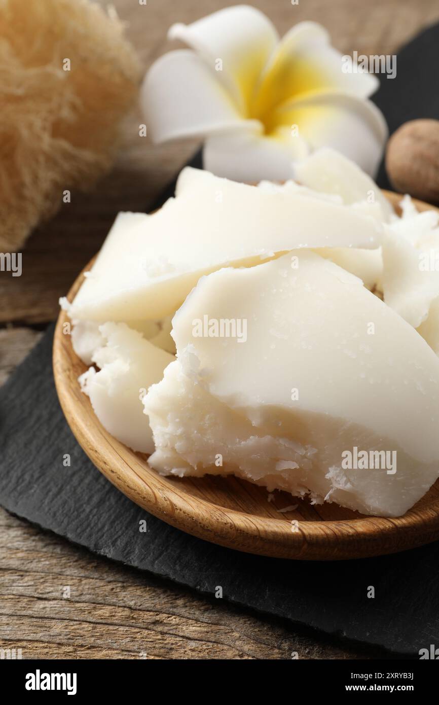 Burro di karité naturale, noci, fiori di plumeria e spugna di loofah su tavola di legno Foto Stock