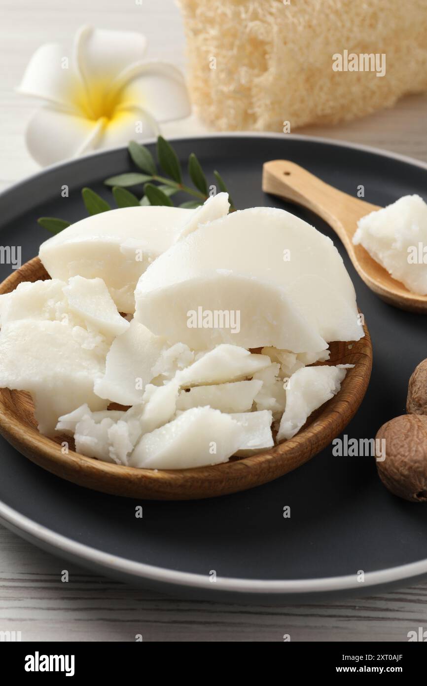 Burro di karité naturale, noci, fiori di plumeria e spugna di loofah su tavola di legno Foto Stock