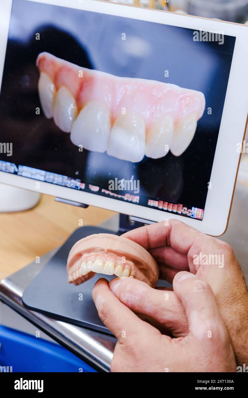 Odontotecnico che esamina una protesi dentale ad arco completo contro un rendering digitale sullo schermo di un computer. Foto Stock