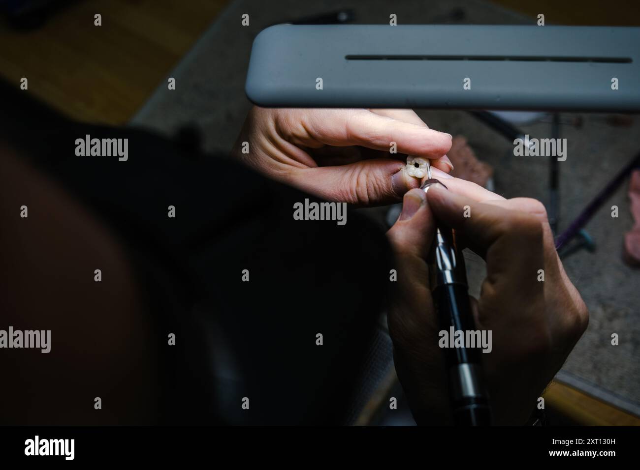 Dall'alto, primo piano irriconoscibile di mani che incidono minuziosamente un piccolo oggetto utilizzando strumenti di precisione, catturati dall'alto. Foto Stock