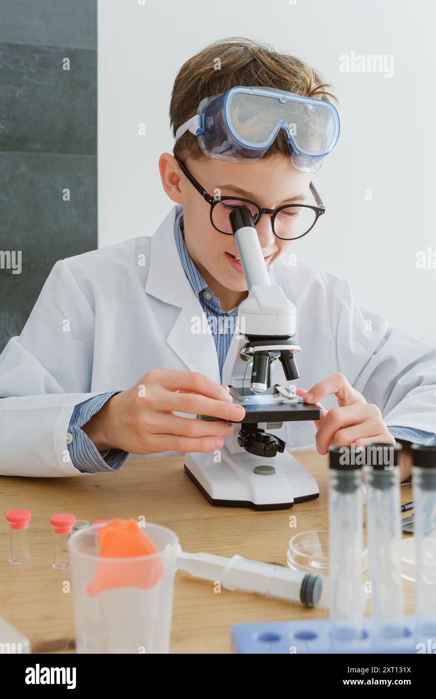 Preadolescente che indossa una provetta per l'esame con il microscopio mentre siede a tavola e si prepara alla ricerca in laboratorio a scuola in classe Foto Stock