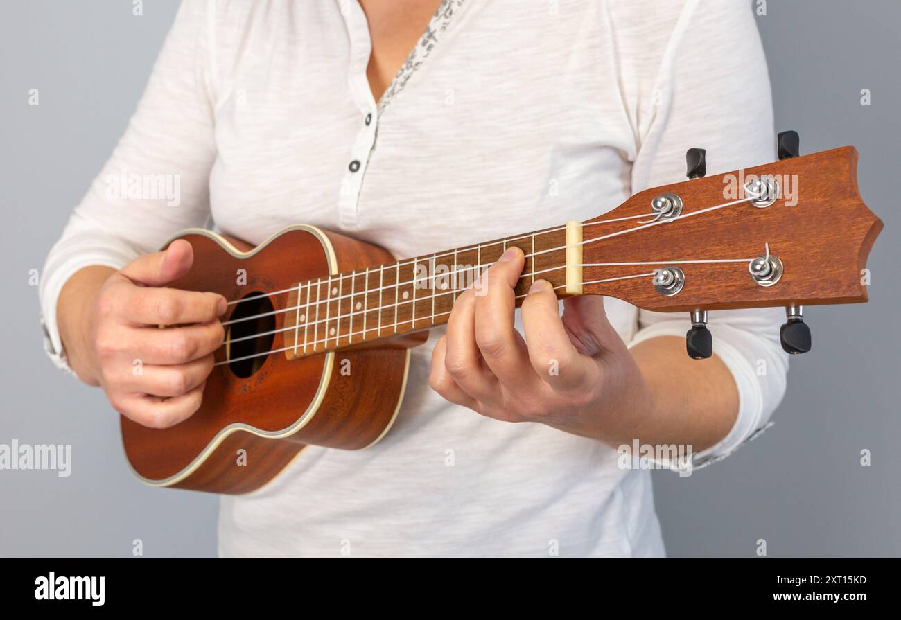 Primo piano anonimo di mani che suonano abilmente accordi su un ukulele, mostrando l'arte della musica e degli strumenti a corda Foto Stock