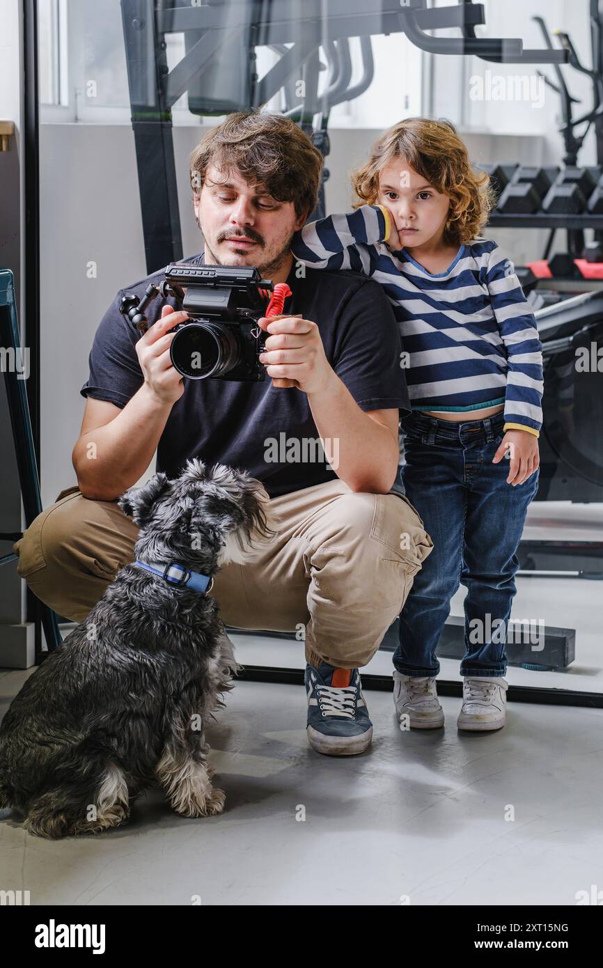 Padre e bambino accompagnati dal loro cane che rivedono i filmati su una videocamera professionale in un ambiente interno Foto Stock