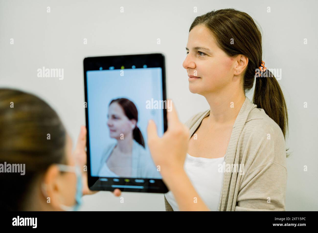 Donna che esamina il suo profilo facciale su un tablet digitale durante un consulto cosmetico Foto Stock