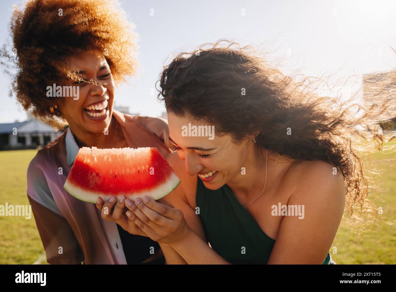 Due migliori amiche che ridono e si godono una soleggiata giornata estiva nel parco con una succosa fetta di anguria. Foto Stock