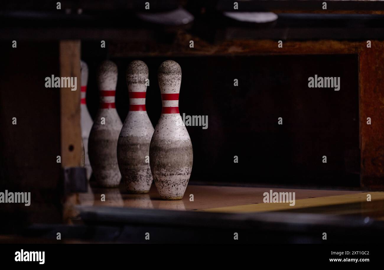 Ripresa ravvicinata di quattro birilli usurati in fila all'interno di una pista da bowling poco illuminata con riflessi sul pavimento che creano un effetto d'atmosfera Foto Stock