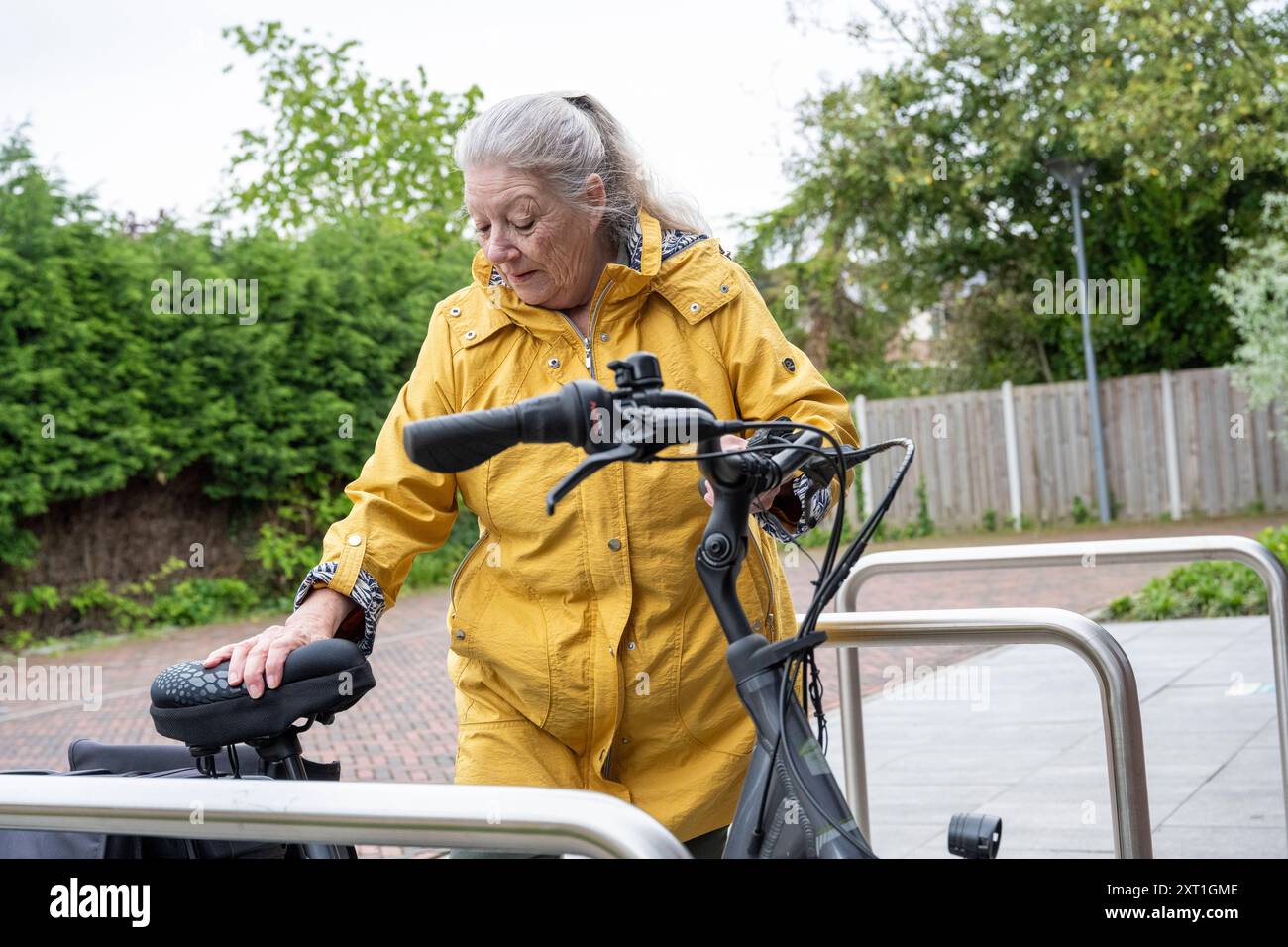 Op de fiets onderweg in una donna anziana in una giacca gialla che fissa la sua bicicletta in un parco urbano. Molenhoek Nederland DEL 202406061 Foto Stock